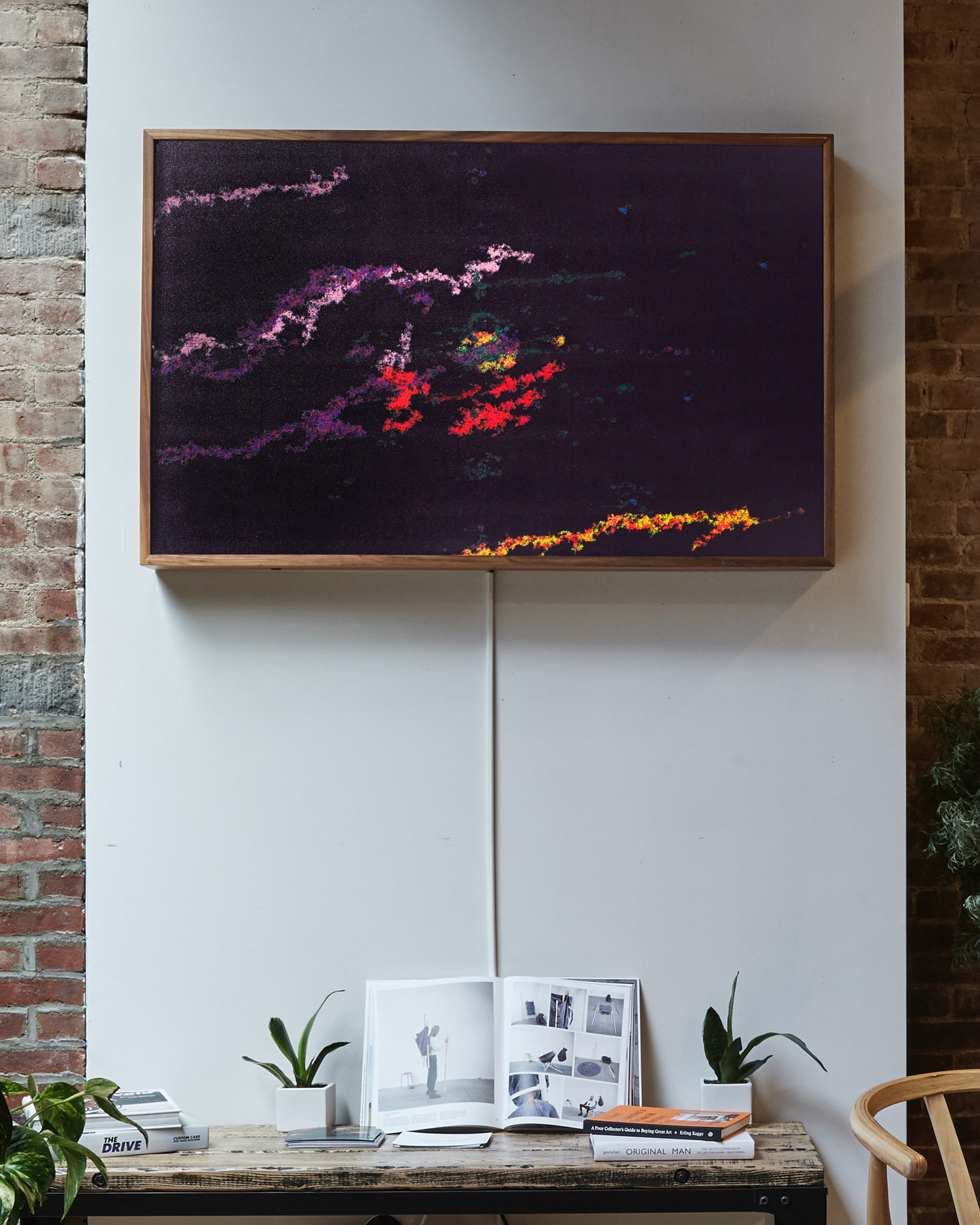 Close-up photograph taken inside a cafe with a framed artwork hanging on a white wall over a desk.